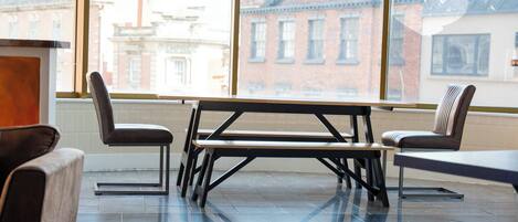 A modern dining area with a table and chairs, large windows with a city view, and a tiled floor.
