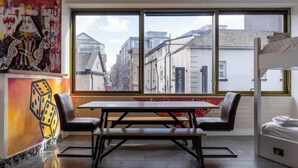 Ein Zimmer mit großem Fenster, einem Holztisch und Bänken sowie einem Bett.