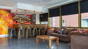 Eine moderne Lobby mit einem 'Welcome to Fabulous Las Vegas'-Schild, einer Bar mit Hockern, einer Sitzecke mit Sofa und einem Holztisch.
