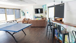 Ein Zimmer mit Tischtennisplatte, einer Couch, einer Bar und einem an der Wand befestigten Fernseher.