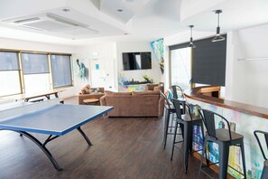 A room with a ping pong table, a sofa, a bar area, and a TV mounted on the wall. - New York Party Pad (Sleeps 16) (Liverpool)