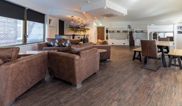 A modern interior with leather sofas, a dining area, and a view through large windows. - New York Party Pad (Sleeps 16) (Liverpool)