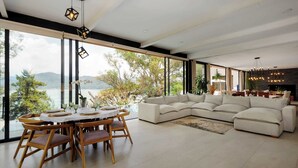 Ein modernes Wohnzimmer mit großem Fenster, einem weißen Sofa, einem Esstisch mit Stühlen und Pendelleuchten.