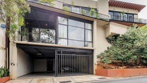 En moderne bygning med to etager, en garage, store vinduer og en balkon med planter.