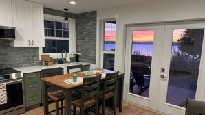 A modern kitchen with a dining area, a view of the outdoors, and a sliding glass door. - Stunning Bluff Cottage with Panoramic Puget Sound & Olympic Mountain Views (Seattle)