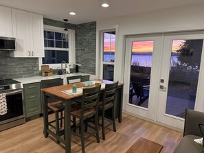A modern kitchen with a dining area, a view of the outdoors, and a sliding glass door. - Stunning Bluff Cottage with Panoramic Puget Sound & Olympic Mountain Views (Seattle)