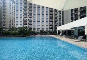 Ein Schwimmbecken mit Liegestühlen und Sonnenschirmen, umgeben von einem Hochhaus mit Balkonen.