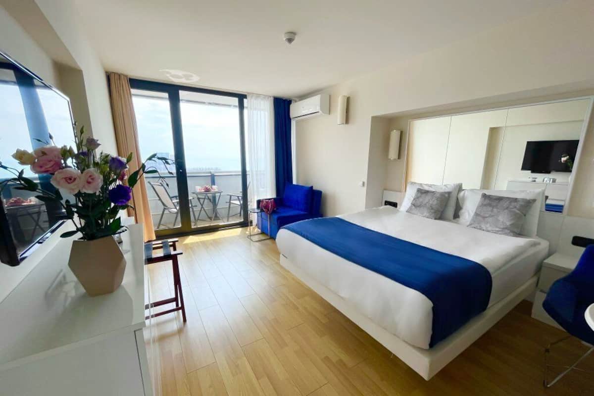 Une chambre d’hôtel moderne dotée d’un grand lit, d’un balcon avec vue, d’un bureau avec un ordinateur et d’une télévision.