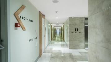 A hotel corridor with a modern design, featuring a marble floor, a wooden directional sign, and a number 11 elevator.