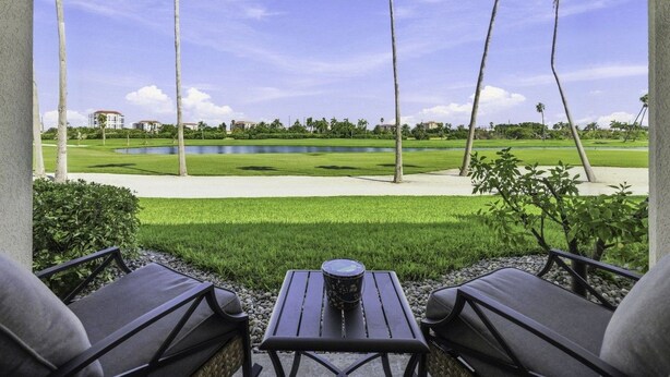 Een overdekt terras met uitzicht op een golfbaan en een waterpartij.