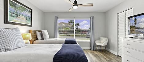 Un dormitorio con dos camas, ventilador de techo, televisión y ventana con cortinas.