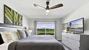 Een slaapkamer met een bed, een plafondventilator, een televisie en uitzicht op een golfbaan.
