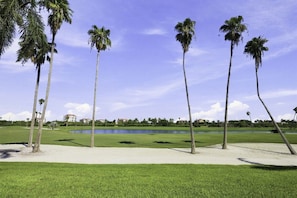 Un parcours de golf bordé de palmiers, avec un étang et des bâtiments en arrière-plan.