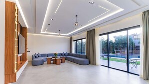 Un salon moderne avec un canapé d’angle, un téléviseur à écran plat et une grande porte-fenêtre coulissante donnant sur une terrasse.