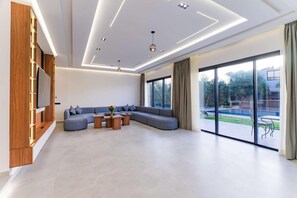 Ein modernes Wohnzimmer mit einer Eckcouch, einem Flachbildfernseher und einer großen Schiebeglastür zu einer Terrasse.