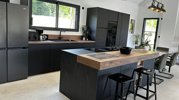 Een moderne keuken met een centraal eiland, zwarte kastjes en hanglampen.