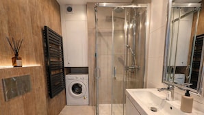A modern bathroom with a glass-enclosed shower, a built-in washing machine, and a large mirror. - Skylight Loft in City Center with AC (Kraków)