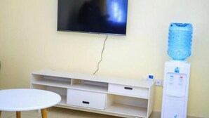 Una stanza con una TV a schermo piatto montata a parete, un mobile bianco contenitore con cassetti, un tavolino rotondo e un distributore d'acqua.