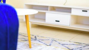Un soggiorno con una TV a schermo piatto montata a parete, un mobile TV bianco sottostante e un tappeto decorato sul pavimento.