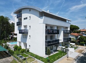 A modern multi-story building with balconies, a swimming pool, and a well-maintained garden. - Cozy Flat With Garden and Pool (San Michele al Tagliamento)