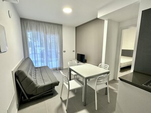 Ein moderner, kompakter Wohnraum mit Sofa, Esstisch, St ühlen, Fernseher und Bett.
