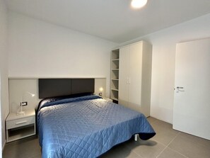 A bedroom with a bed, bedside table, wardrobe, and a door. - Cozy Flat With Garden and Pool (San Michele al Tagliamento)