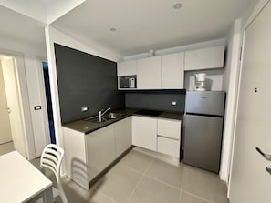 Eine kleine Küche mit weißen Schränken, einem Edelstahlkühlschrank, einer Mikrowelle und einem Spülbecken.