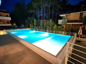 A rectangular swimming pool with a white border and a tiled deck area. - Cozy Flat With Garden and Pool (San Michele al Tagliamento)