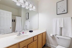 Une salle de bain avec un lavabo blanc, des meubles en bois, un grand miroir, des toilettes et un tableau encadré au mur.