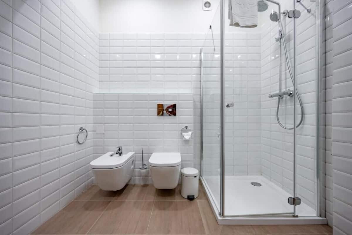 Un baño moderno con azulejos blancos tipo metro, ducha con cerramiento de vidrio, un bidé y un inodoro.