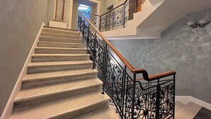 Una escalera con escalones de mármol y barandillas de hierro forjado negro que conduce a un rellano con una araña.