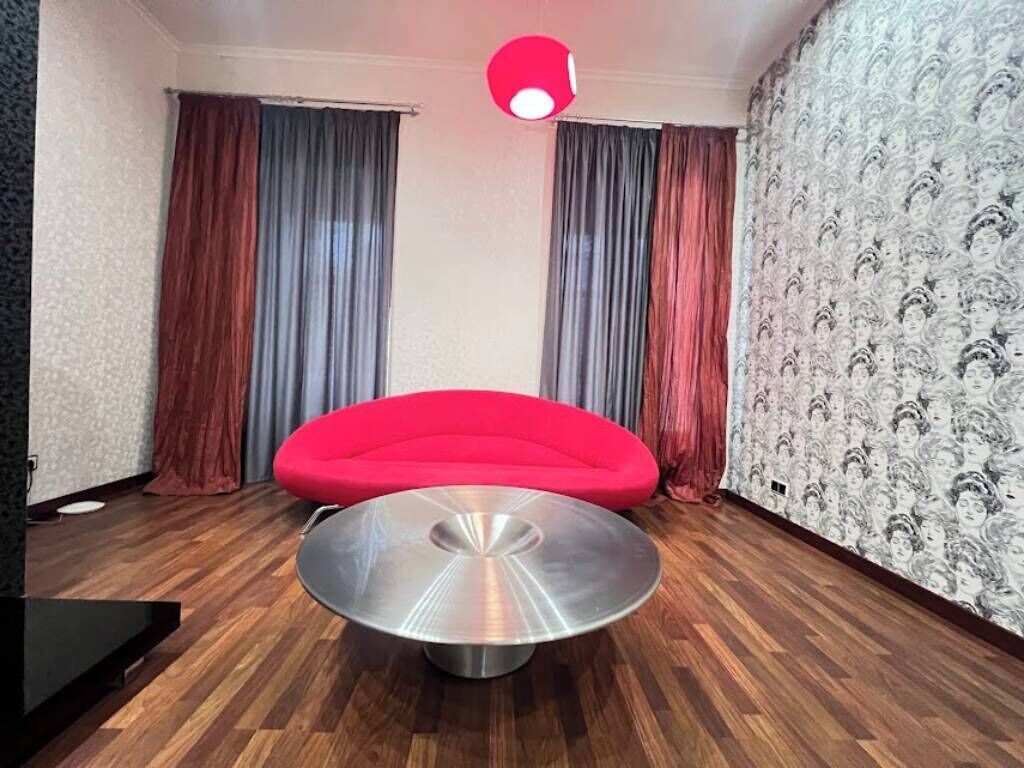 A room with a red sofa, a round metallic table, and patterned wallpaper.