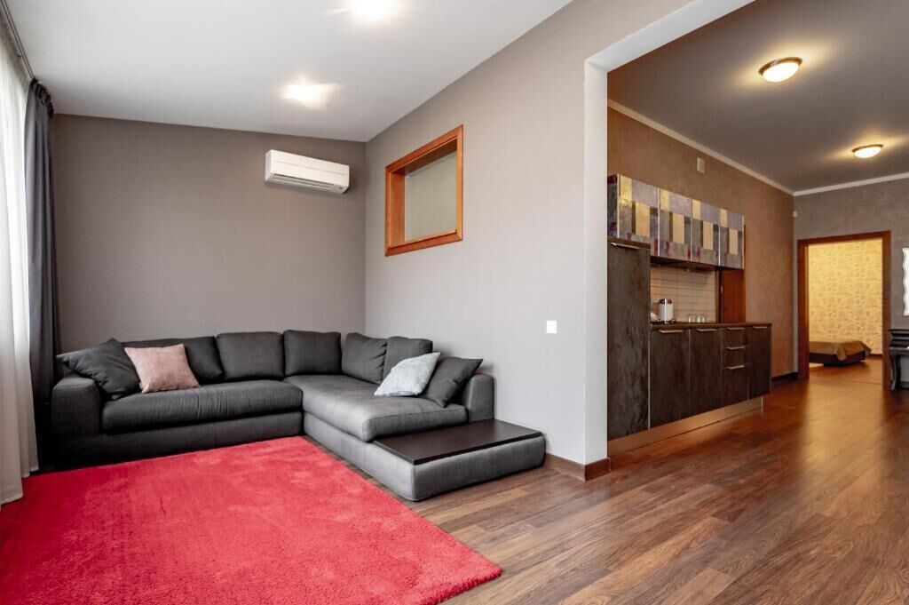 A modern living room with a sectional sofa, a red rug, and a kitchen area with wooden cabinets.