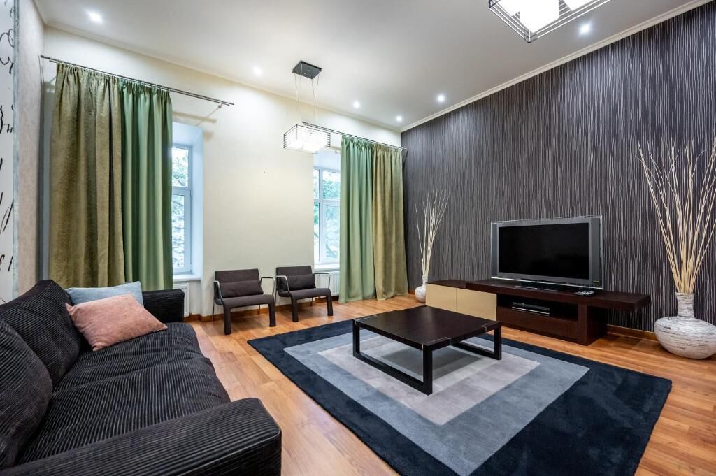 A modern living room with a sofa, chairs, a TV, and a large window with curtains.