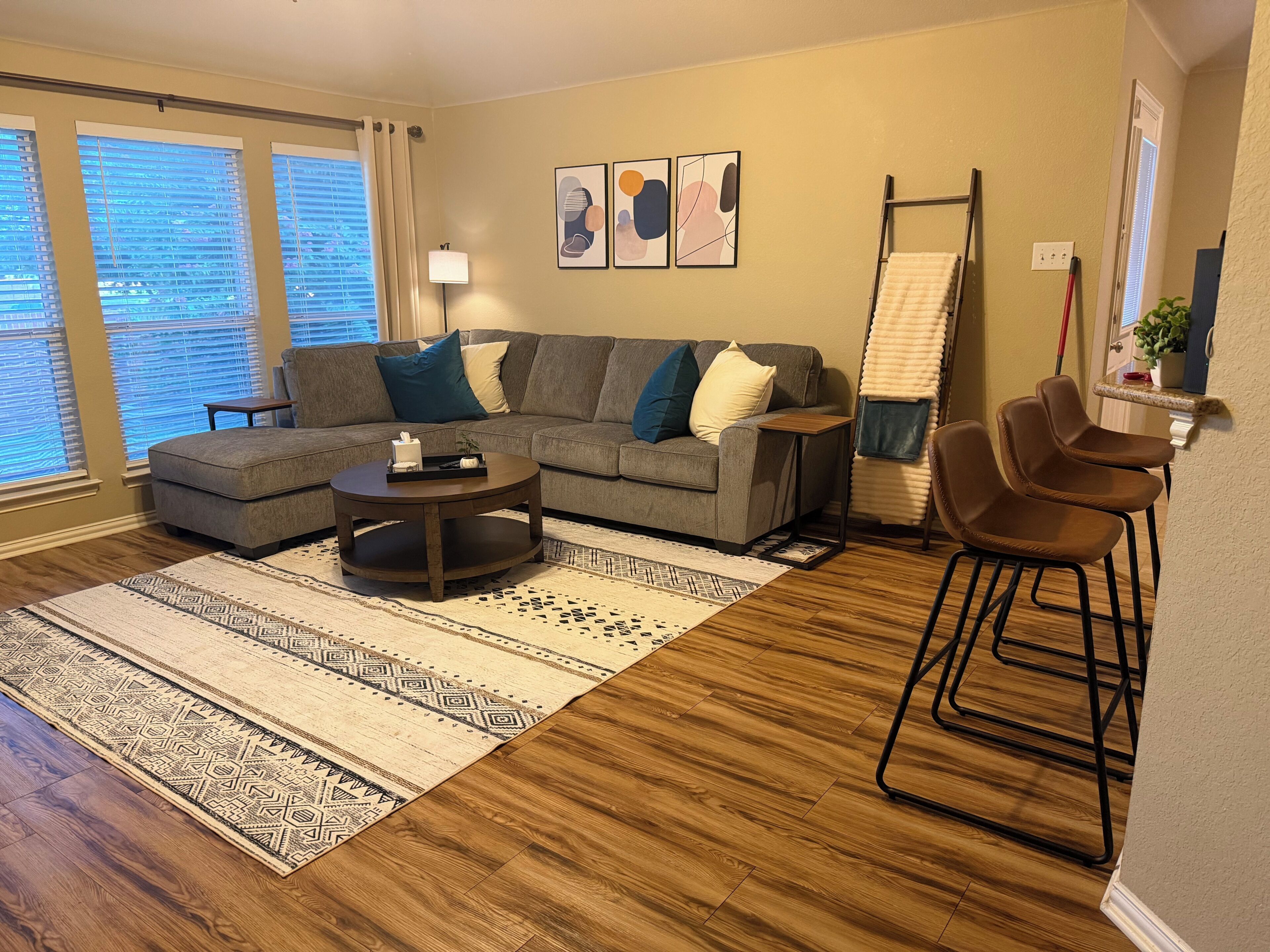 A living room with a sectional sofa, a coffee table, a patterned rug, and a bar stool.