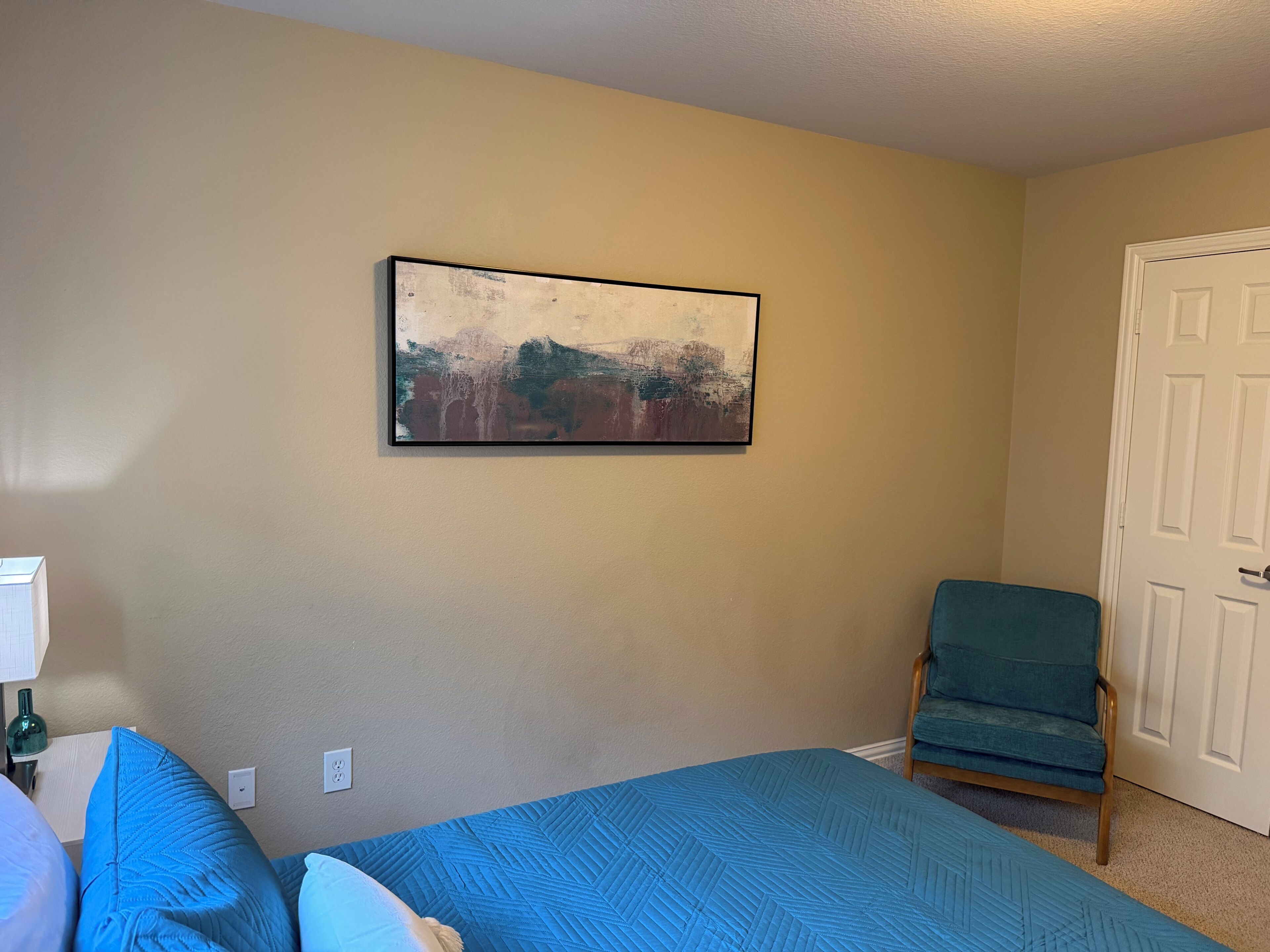 A room with a bed, a chair, and a painting on the wall.