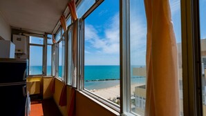 A room with a large window overlooking a beach, a radiator, and a door. - GuestHost - Sea View Europa Apartment (Montesilvano)