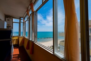 A room with a large window overlooking a beach, a radiator, and a door. - GuestHost - Sea View Europa Apartment (Montesilvano)