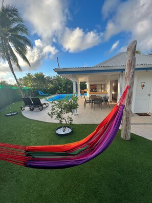Ein Garten mit Pool, Gartenmöbeln, einer Hängematte und einem Haus, dessen Küche sichtbar ist.