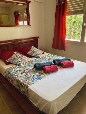 Ein Bett mit floraler Bettdecke, roten Kissen und blauen Handtüchern mit Text.
