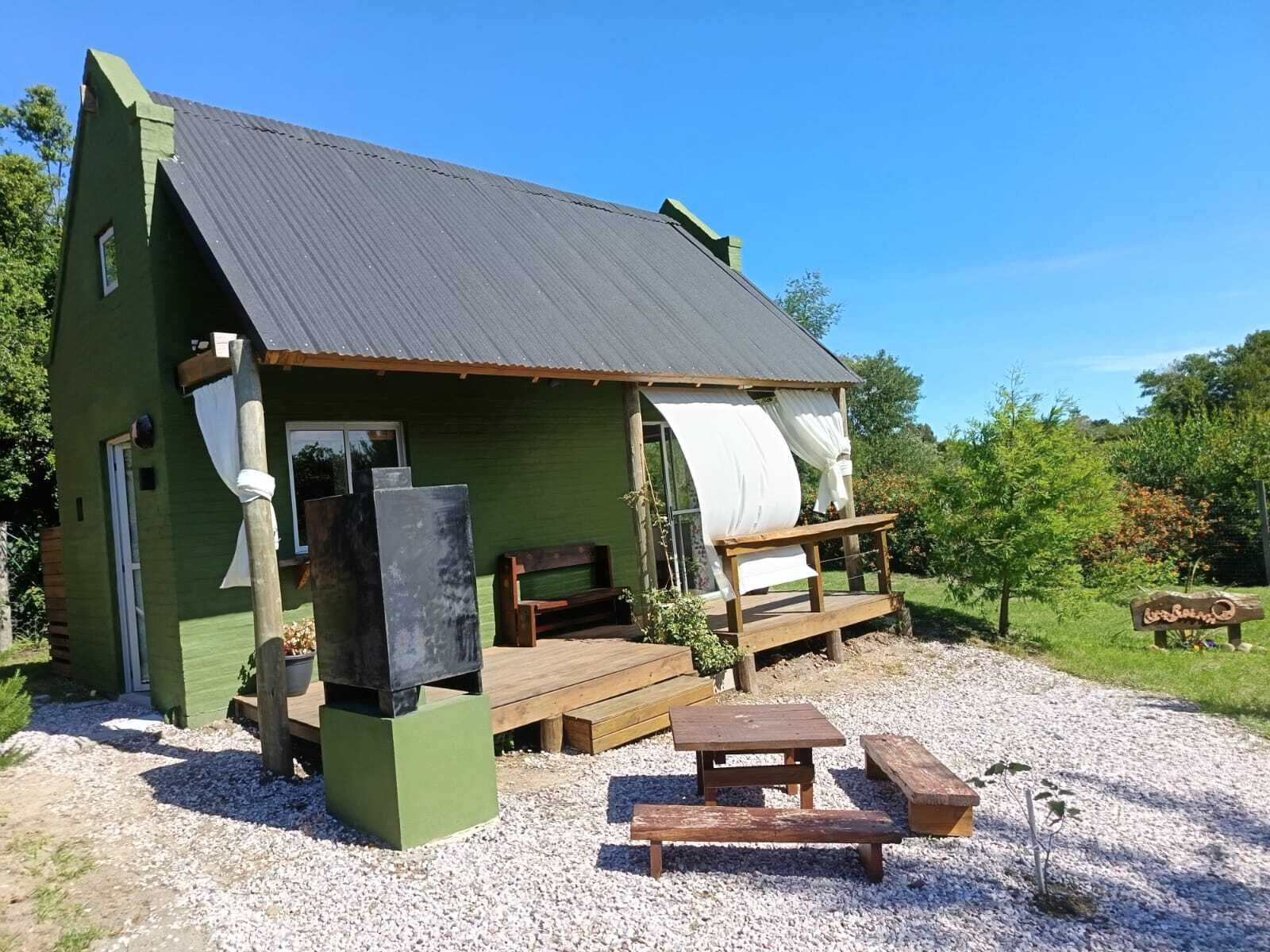 Eine kleine, grüne Holzhütte mit Metall-Dach, einer Holzterrasse und einem Picknicktisch.