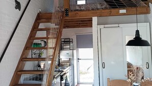 Ett lantligt kök med en trätrappa, en hängande lampa och utsikt över matplatsen.