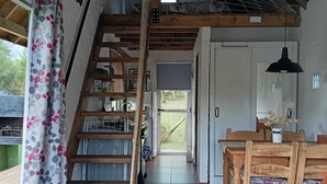 En rustik inredning med en trätrappa, ett matområde och utsikt genom en dörr.