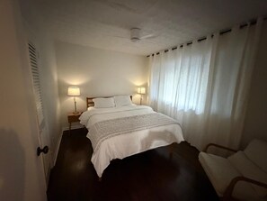 Ein Hotelzimmer mit Bett, Nachttischlampen, einem Sessel und einem Fenster mit Vorhängen.