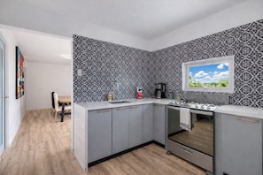 Een moderne keuken met grijze kastjes, een inbouwoven en een raam met uitzicht op de lucht.