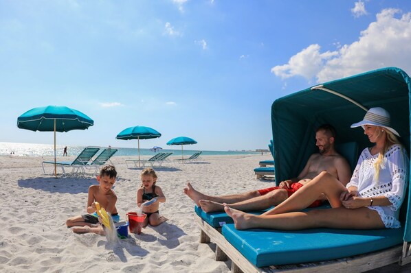 Une scène de plage avec un espace de repos abrité, des chaises de plage et des parasols.