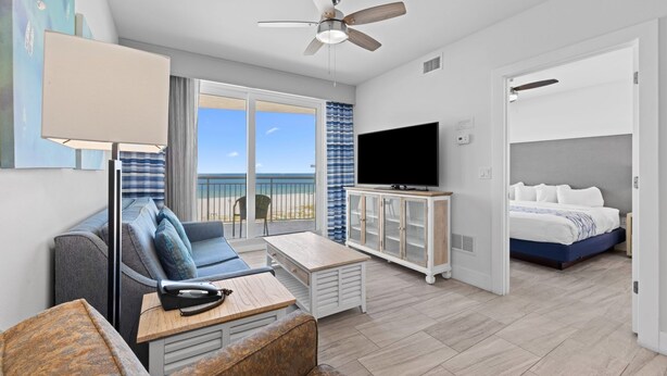 Een moderne hotelkamer met balkon, flatscreen televisie, een bank, salontafel en bed.