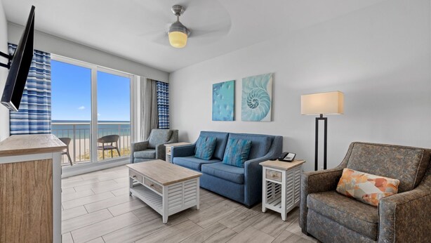 A modern living room with a sofa, armchair, coffee table, and a TV mounted on the wall. - Premium Corner Suite w/ Gulf Views | Beach & Pool (Treasure Island)