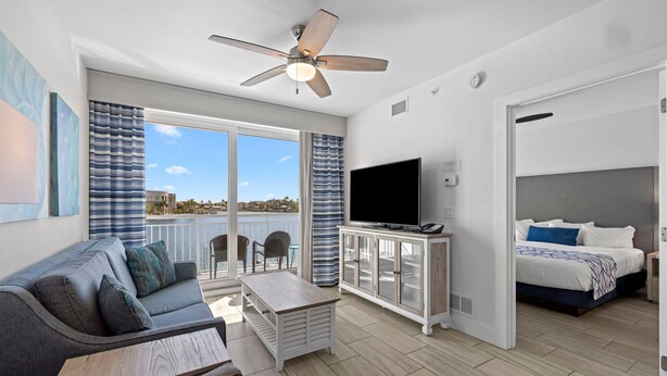 A modern room with a sofa, TV, and a balcony with a view. - 2BR Bayfront Suite w/ Marina Views | Pools & Beach (Treasure Island)