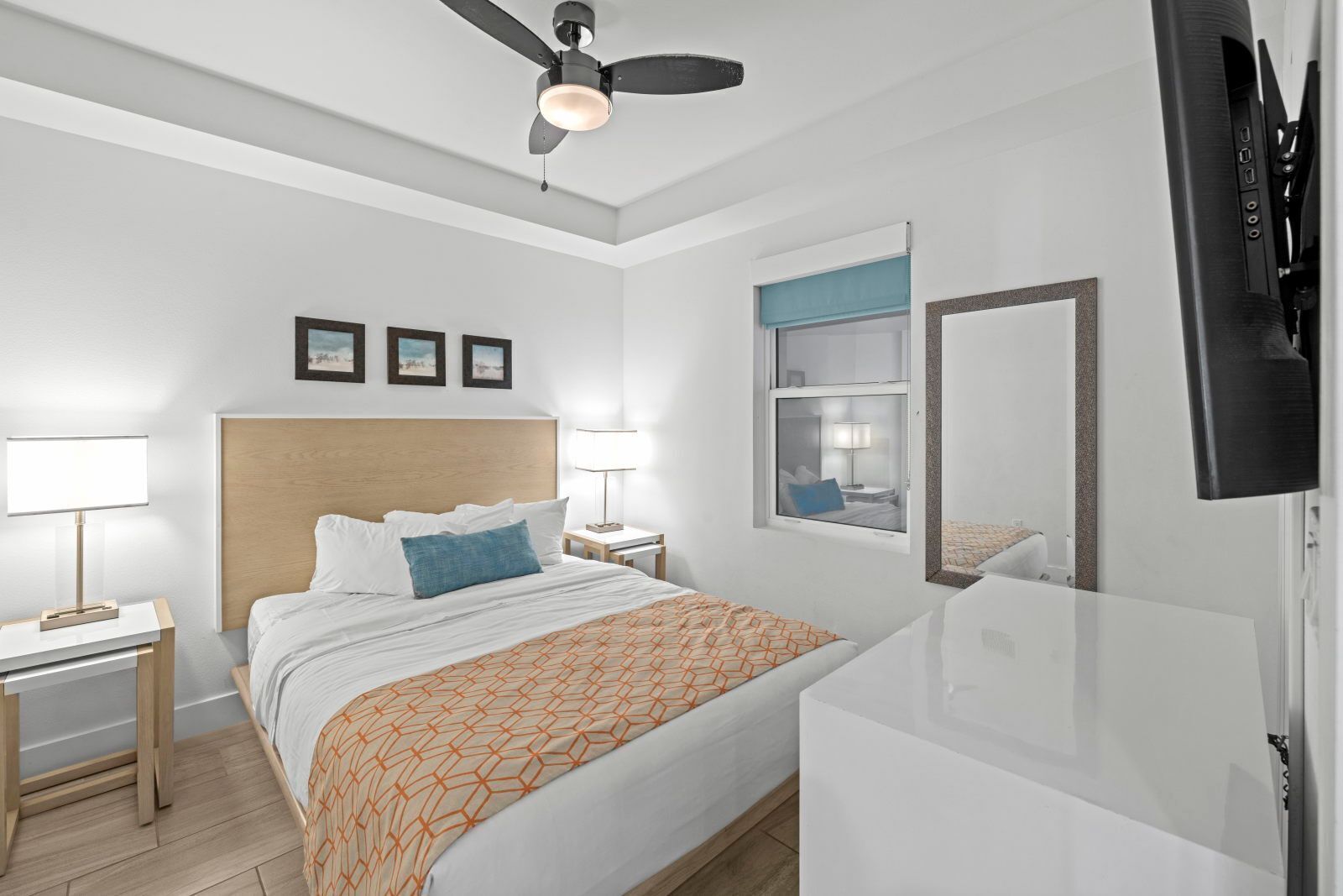 Ein modernes Hotelzimmer mit Bett, Nachttischen, Deckenventilator, Fernseher und Fenster.